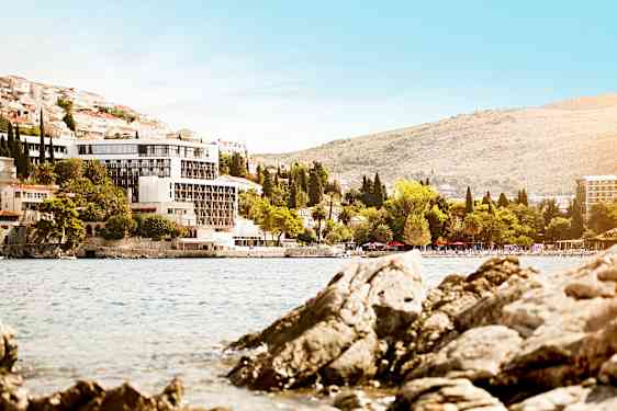 Vy mot en byggnad vid en kustlinje med stenig strand och gröna träd. (AI-genererad text)