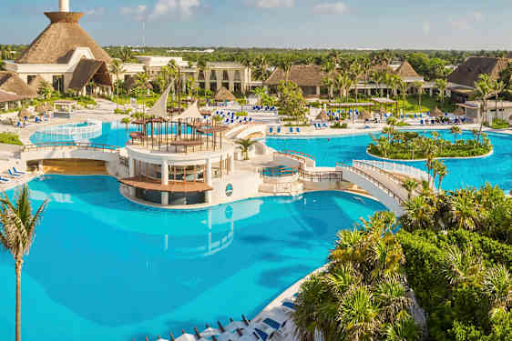 En stor pool med broar och ett centralt område omgivet av tropiska växter och byggnader. (AI-genererad text)