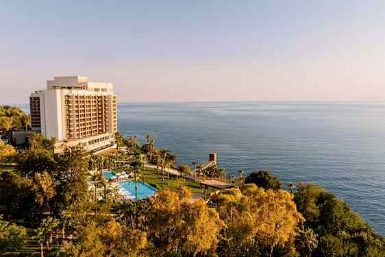 Hotellbyggnad med pool och grönska framför havet. (AI-genererad text)