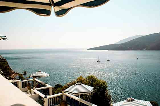 Bild av havsutsikt med solreflektioner, segelbåtar och terrass med parasoll. (AI-genererad text)