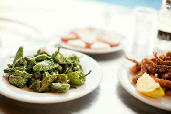 Rätter med gröna paprikor, skaldjur med citron och skivad ost med tomat serveras på vita tallrikar. (AI-genererad text)