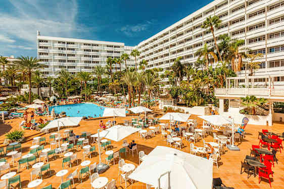 Hotell med stor utomhusterrass, poolområde och palmer. (AI-genererad text)