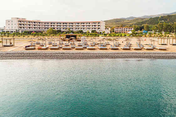 Strand med solstolar och parasoller framför ett hotell. (AI-genererad text)