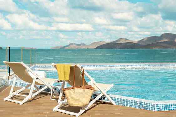 Två solstolar vid en pool med utsikt över havet och berg i bakgrunden. (AI-genererad text)