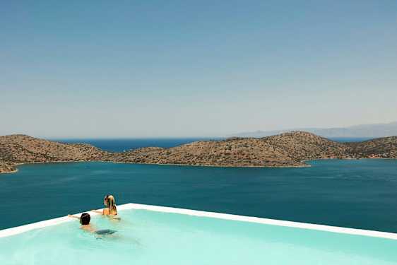 Två personer i en infinitypool med utsikt över havet och berg i bakgrunden. (AI-genererad text)