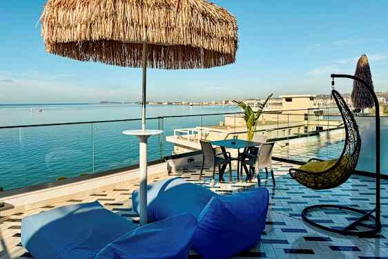 En takterrass med utsikt över havet, med sittplatser, ett parasoll och en hängstol. (AI-genererad text)