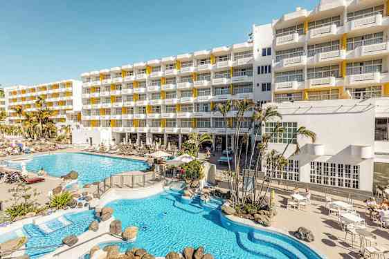 Hotellbyggnad med solstolar och poolområde. (AI-genererad text)