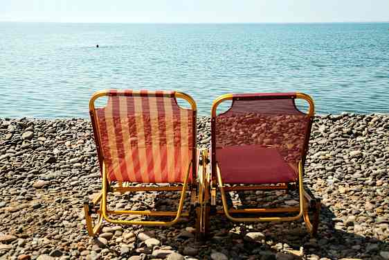 Två solstolar står på en stenig strand framför havet. (AI-genererad text)