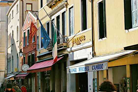 Fasad av byggnader med en italiensk flagga, europeisk flagga och skyltar som anger hotell och växling. (AI-genererad text)