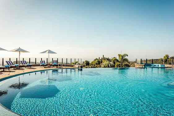 Utomhuspool med solstolar och parasoller kring kanten, samt utsikt över landskap med vegetation. (AI-genererad text)