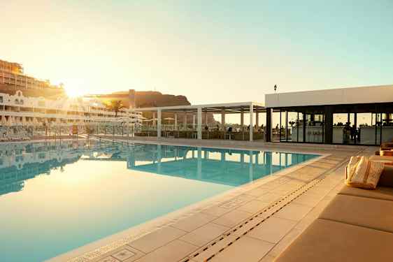 Utomhuspool vid ett hotell med solstolar och en byggnad i bakgrunden. (AI-genererad text)