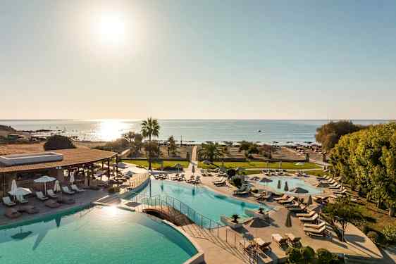 Utsikt över en poolområde med solsängar och parasoller, samt stranden och havet i bakgrunden. (AI-genererad text)