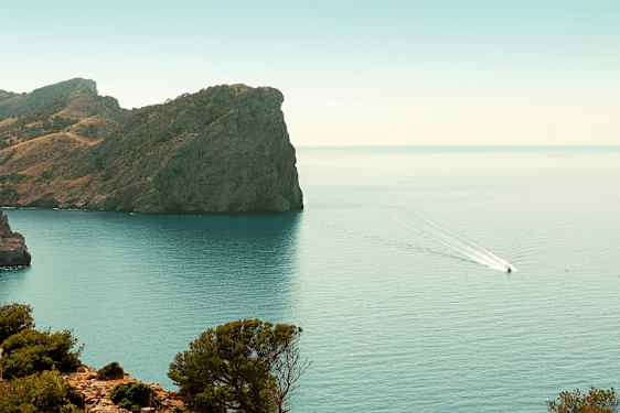 En klippa vid en kust med en båt som kör på vattnet. (AI-genererad text)