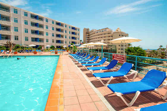 En utomhuspool med solstolar och parasoller vid sidan, omgiven av hotelbyggnader. (AI-genererad text)