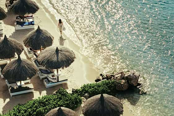 En sandstrand med parasoller och solstolar bredvid ett klart hav. (AI-genererad text)