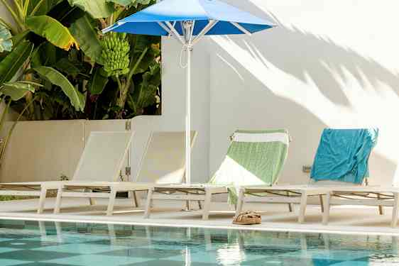 Solstolar och parasoll vid poolen, med bananplantor i bakgrunden. (AI-genererad text)