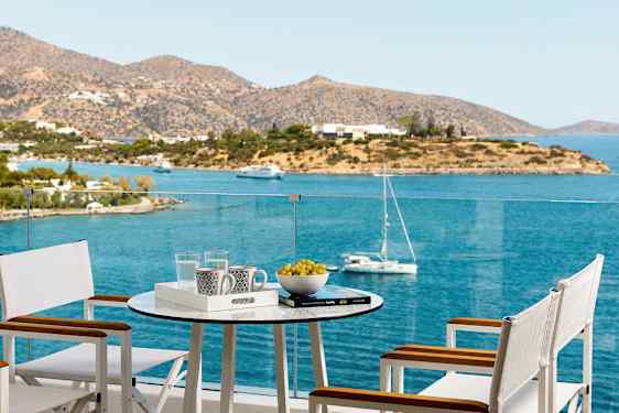 En terrass med bord och stolar med utsikt över havet och en ö. (AI-genererad text)