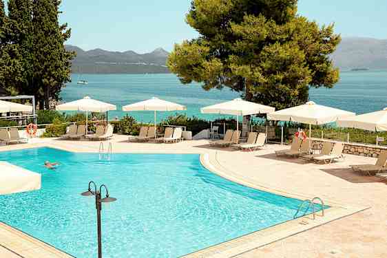Utomhuspool med parasoller och solstolar, i bakgrunden syns havet och berg. (AI-genererad text)