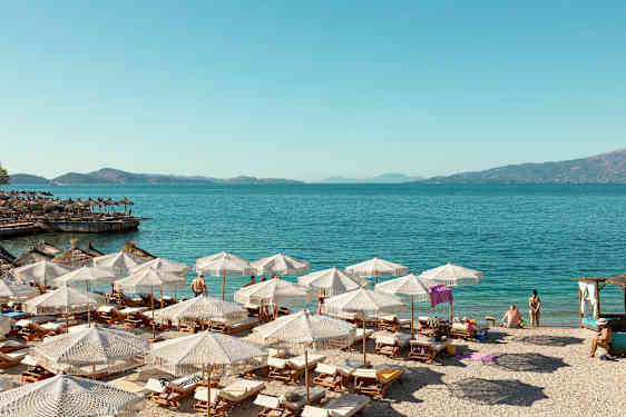 Strand med solstolar och parasoller vid klart blått vatten. (AI-genererad text)