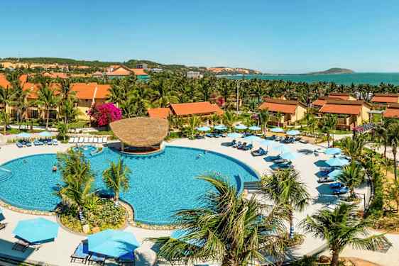 Semesteranläggning med stora byggnader med tegeltak, palmer och en pool i centrum. (AI-genererad text)