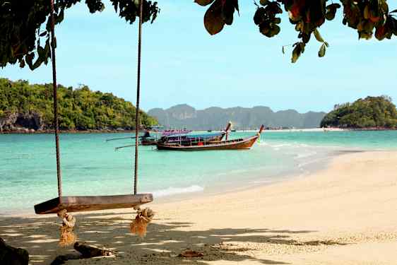 Strand med gunga och en träbåt på vattnet framför skogsklädda öar. (AI-genererad text)