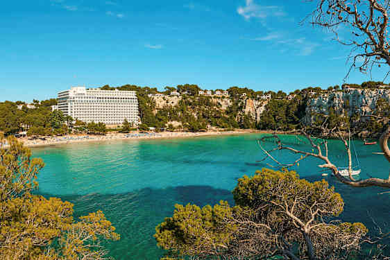 En strand med en resortbyggnad och grönskande branter vid ett turkost hav. (AI-genererad text)