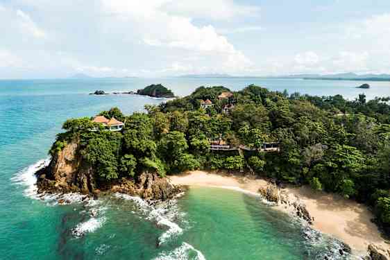 En kustlinje med gröna träd och villor syns bredvid en sandstrand och klart turkost hav. (AI-genererad text)