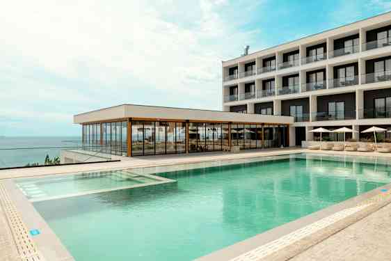 Ett hotell med modernt poolområde och havsutsikt. (AI-genererad text)