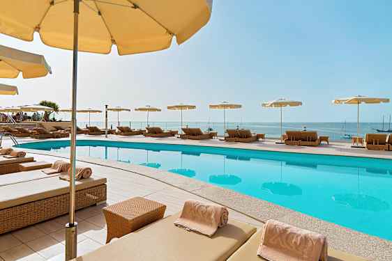 Solstolar med parasoller kring en pool, och utsikt över havet. (AI-genererad text)