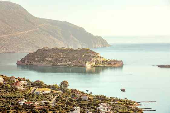 En vy över en historisk ö med ruiner och omgivande hav, och i förgrunden syns en kuststad med byggnader. (AI-genererad text)