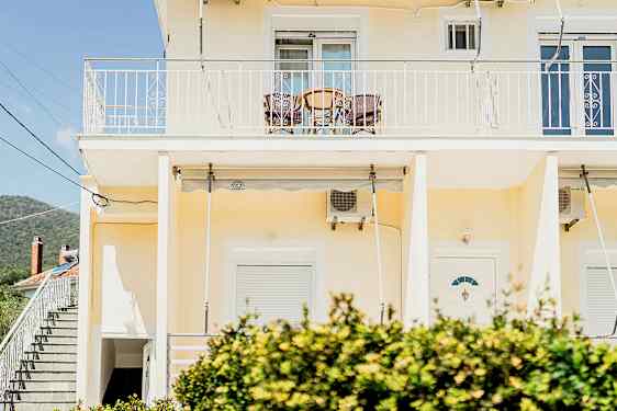 En gul byggnad med en balkong högst upp och buskar i förgrunden. (AI-genererad text)