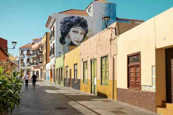 Färgglada husfasader längs en gångväg med två personer som promenerar. (AI-genererad text)