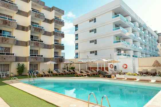 Hotellbyggnader vid en utomhuspool omgivna av solstolar och parasoller. (AI-genererad text)