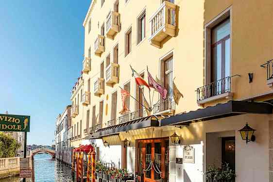 En gul byggnad med balkonger längs en kanal, med en gångbro i bakgrunden. (AI-genererad text)