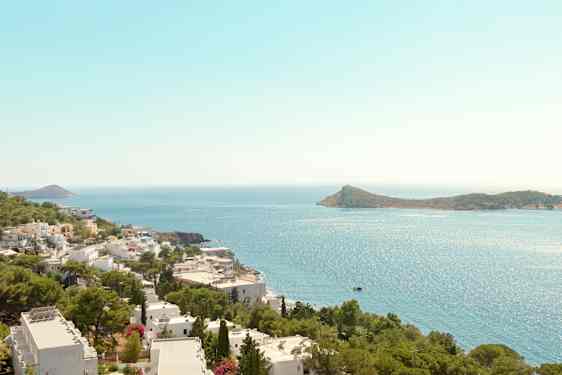 Utsikt över kustlinje med vita byggnader och gröna träd, hav och en ö i bakgrunden. (AI-genererad text)