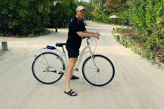 Tomas på cykel på kritvit sandväg mellan grönska