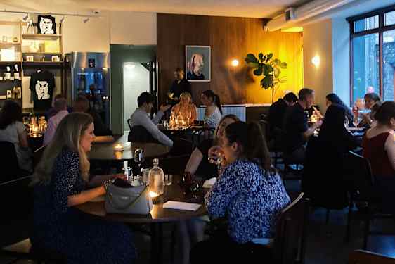 Folk sitter vid bord på en restaurang med dämpad belysning.