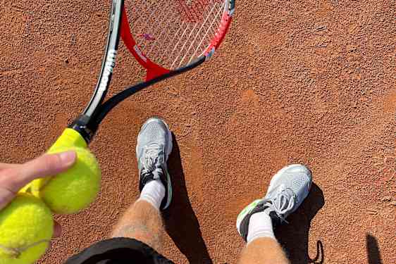 Man håller i en tennisracket och två tennisbollar