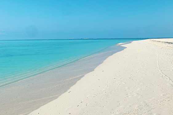 Kritvit sandstrand med turkosblått hav och klarblå himmel