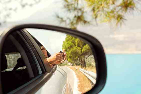 I backspegel på en bil syns en person som lutar sig ut och fotar med mobilen.