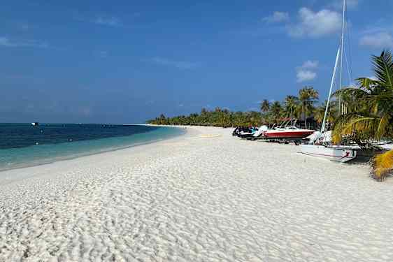 Båtar på kritvit strand och turkostblått hav och palmer