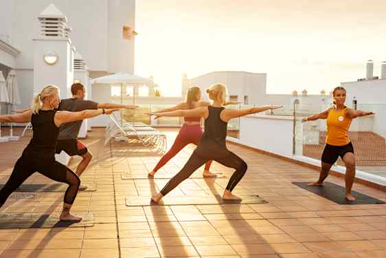 En grupp människor står i yogaposition på en takterrass.