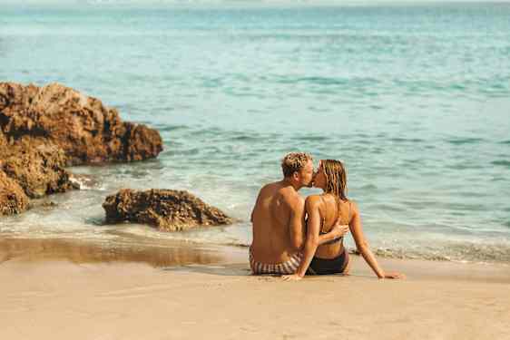 Ett par som sitter på stranden vid vattenbrynet.