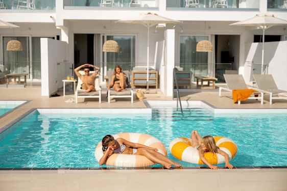 Rum med poolaccess två barn i poolen och förälkdrar i solstolar på terrassen