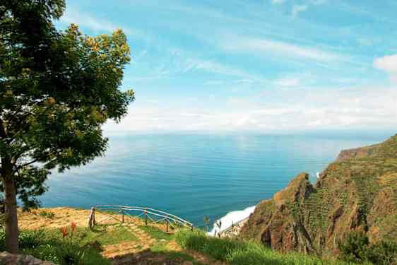Utsikt från ett berg på Madeira över ängar, hav och berg.