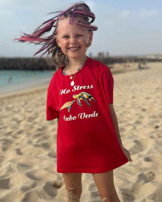 En glad och nöjd flicka i en “no stress”-t-shirt på stranden