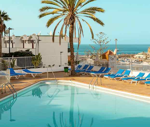 En utomhuspool omgiven av solstolar, med utsikt över havet och omgiven av palmer. (AI-genererad text)