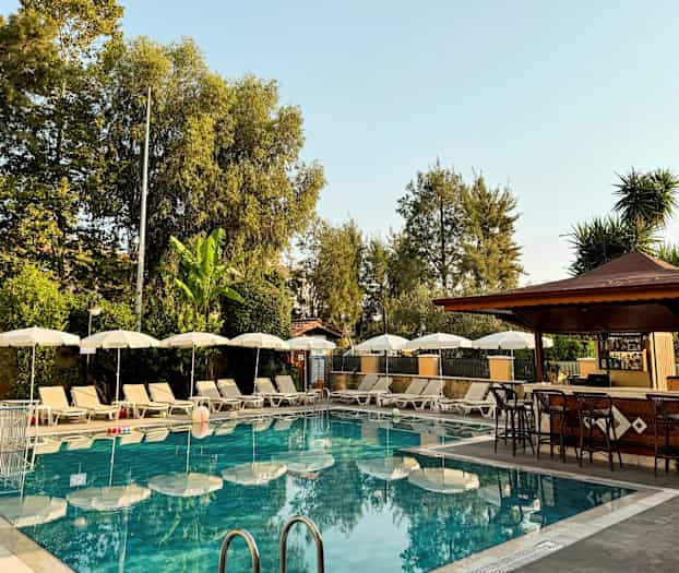 Utomhuspool med solstolar och parasoller bredvid en bar. (AI-genererad text)