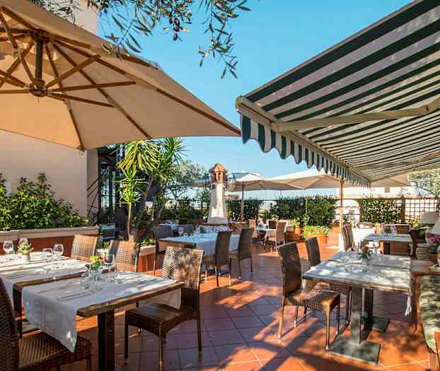 En uteservering med bord och stolar under parasoller och markiser. (AI-genererad text)