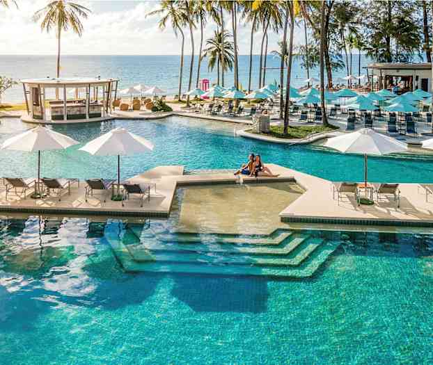 En stor pool med solstolar och parasoller med utsikt mot havet, omgiven av palmer. (AI-genererad text)